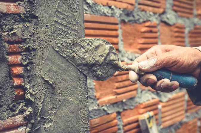 Trowel drawing a smooth parge coat across masonry