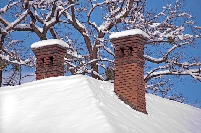 Twin brick chimneys standing above a snow-covered roof